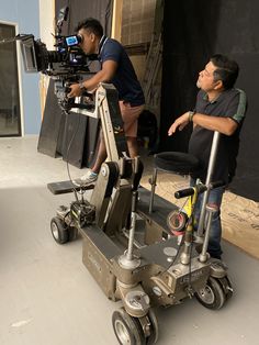 two men standing next to each other in front of a camera on a tripod