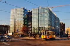 a yellow trolley driving down a city street next to tall buildings with glass windows on each side