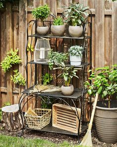 an outdoor garden area with potted plants and gardening implements on a shelf next to a wooden fence