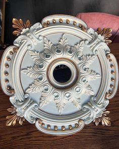 an ornate white and gold plate sitting on top of a wooden table next to a pink chair