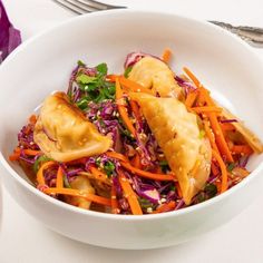 a white bowl filled with vegetables and dumplings on top of a table next to silverware