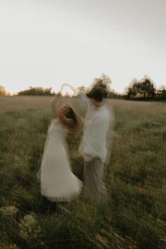 two people standing in a field with one holding the other's hand and dancing