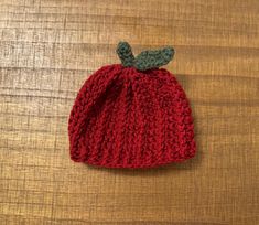 a crocheted red hat with a green leaf on the top sitting on a wooden surface