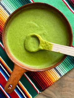 a wooden spoon is in a bowl filled with green liquid on a colorful table cloth