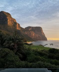 the ocean and mountains are seen at sunset from an outdoor swimming pool in front of it