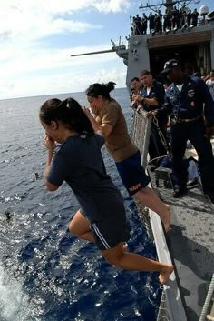 people are on the deck of a ship as an airplane flies overhead