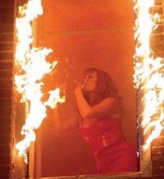 a woman standing in front of a mirror with fire coming out of the window behind her