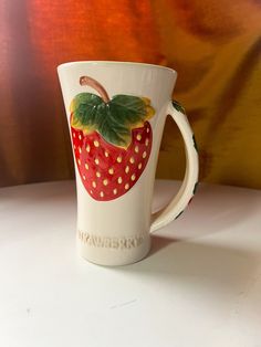 a coffee cup with a strawberry painted on the front and bottom, sitting on a table