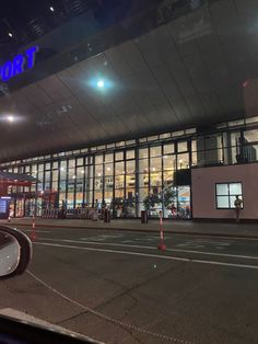 an empty street in front of a large building with lots of windows and lights on it