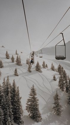 a person riding a ski lift up the side of a snow covered mountain next to trees