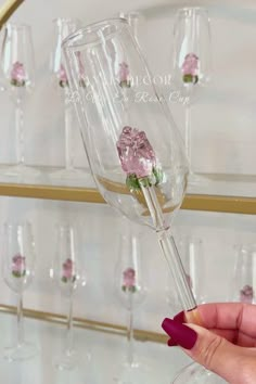 a hand holding a wine glass with pink flowers in it and several other glasses behind it