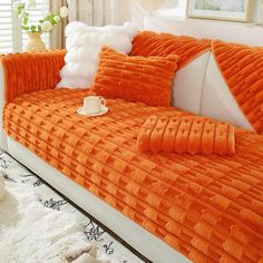 an orange couch with some pillows on top of it and a white rug in front of it