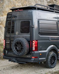 the rear end of a van parked in front of a rocky mountain side with no one on it