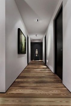 an empty hallway with paintings on the wall and wooden floors in front of it, along with black doors