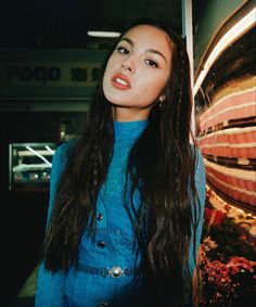 a woman with long hair standing in front of a wall and looking at the camera