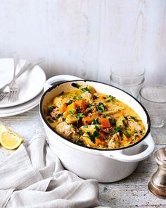 a casserole dish with chicken and vegetables in it on a table next to silverware