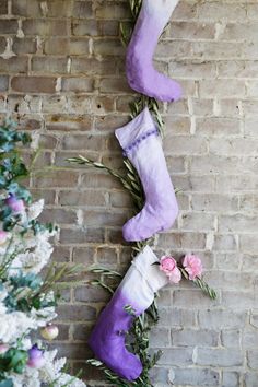 three stockings hanging on a brick wall with pink flowers and greenery around the stocking