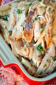 a red and white dish filled with meat covered in gravy on top of a checkered table cloth