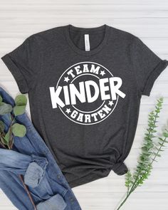 a t - shirt that says team kinder on it next to jeans and flowers