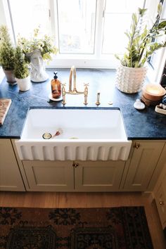 a white sink sitting under a window next to a rug and potted greenery