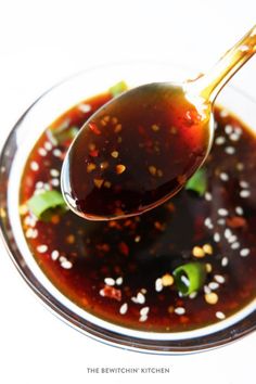 a spoon full of korean barbecue sauce on top of a glass bowl with sesame seeds