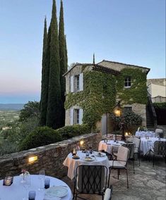 an outdoor dining area with tables and chairs on the side of a stone building, surrounded by greenery