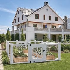 a large house with a white fence surrounding it and some plants in the front yard