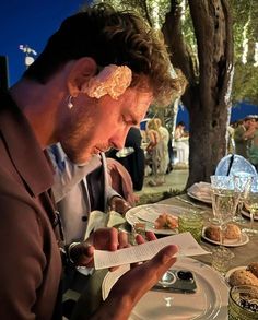 a man sitting at a table with food in front of him and reading a menu