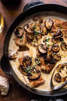 a skillet filled with chicken and mushrooms covered in gravy next to bread