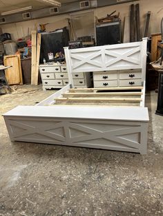 a white bed frame sitting on top of a floor next to dressers and drawers