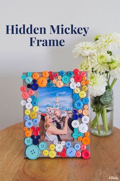 a photo frame sitting on top of a wooden table next to flowers and a vase filled with white flowers