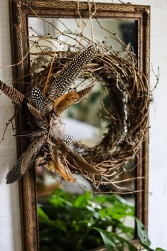 a mirror hanging on the wall next to a wreath with feathers and twigs in it