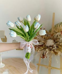 a bouquet of white tulips is being held by a woman's hand