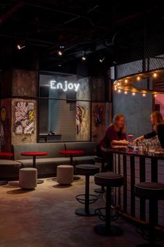 two women sitting at a bar with stools in the foreground and an empty wall behind them