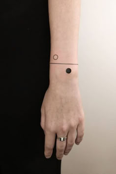 a woman's hand with a small black dot tattoo on her left wrist and an arrow in the middle