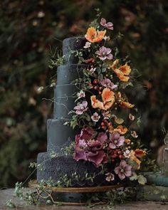 a three tiered cake decorated with flowers and greenery sits on a wooden table