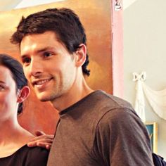 a man and woman standing next to each other in front of a painting on the wall