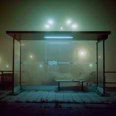 an empty bus stop at night with the lights on and fog covering the glass walls