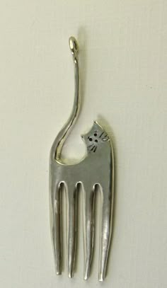 a metal cat shaped fork with a small kitten on it's back end, attached to a wall