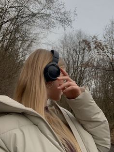 a woman wearing headphones while looking into the distance with trees in the back ground