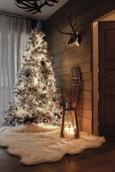 a white christmas tree in front of a window with lights and a deer head on the wall