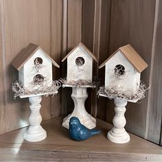 three white bird houses on top of a wooden shelf next to a blue bird statue