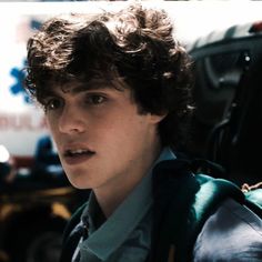 a young man with curly hair wearing a backpack