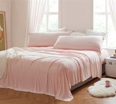 a bed with pink sheets and pillows next to a window