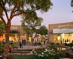 people are walking around in front of a store at dusk with christmas lights on the trees