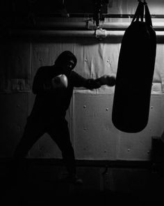 a man in a black hoodie is boxing with a punching bag on the wall