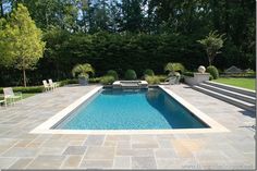 a swimming pool surrounded by stone steps and lawn furniture in a backyard area with trees