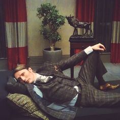 a man in a suit and tie laying on a black couch next to a potted plant