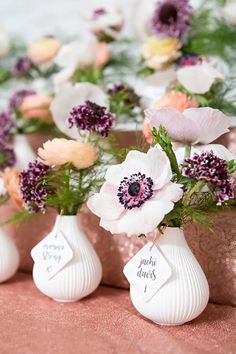 three vases with flowers are sitting on a table together, one has a name tag