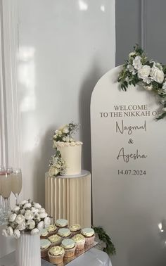 a wedding cake and cupcakes on a table in front of a welcome sign